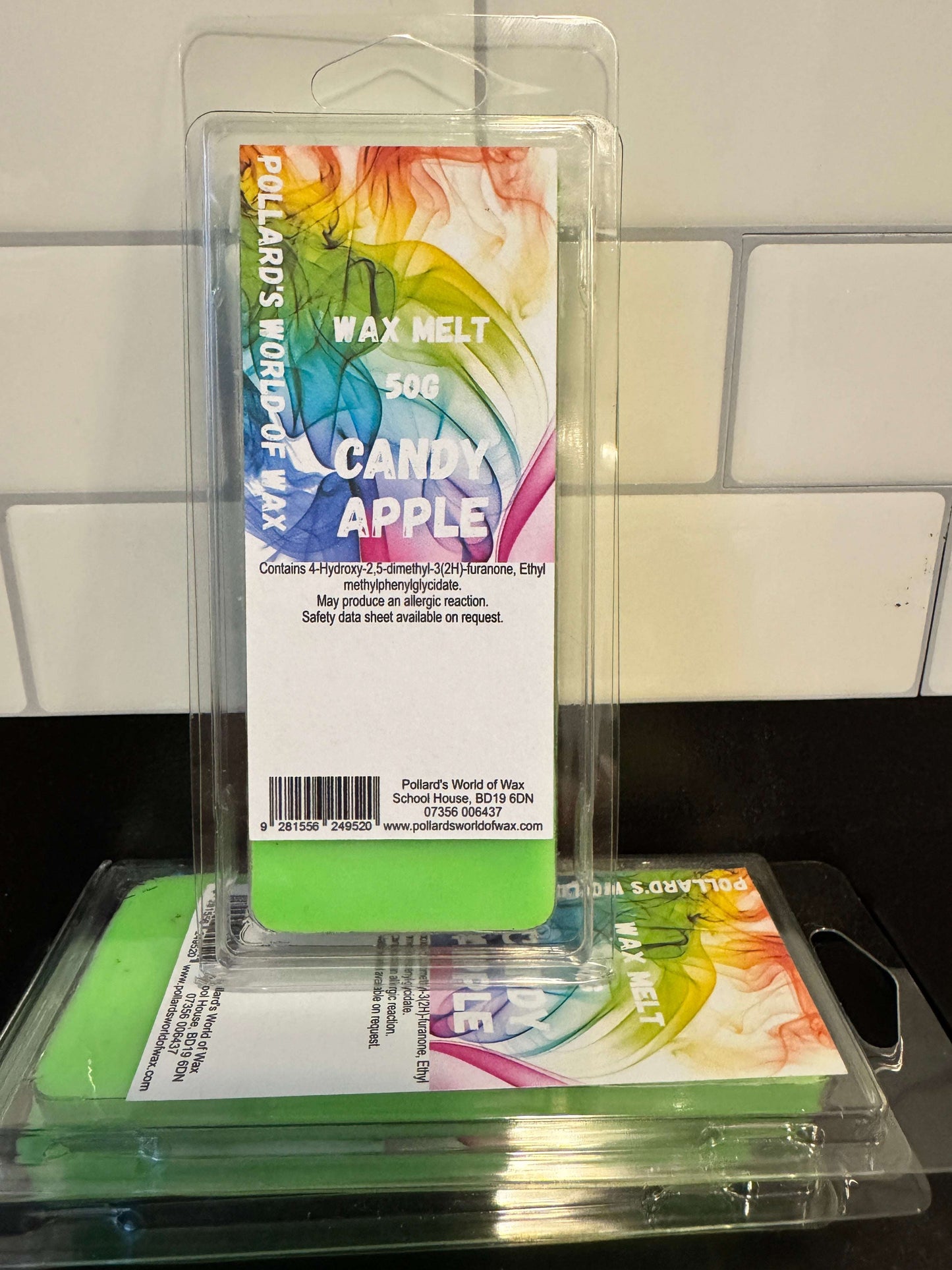 Two wax melts in packaging with colorful labels on a reflective surface.
